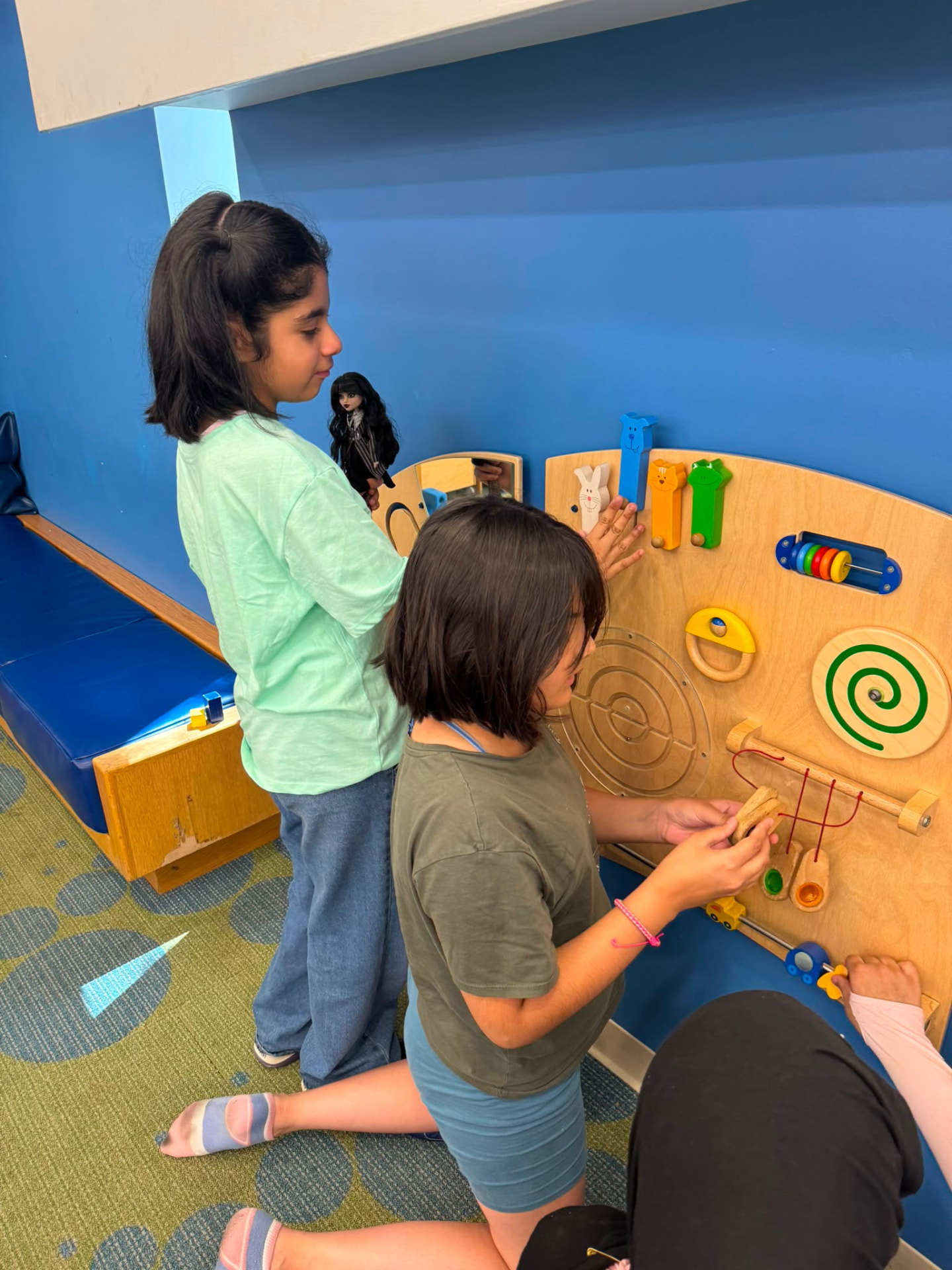 Children exploring a wall-mounted activity board in a blue play space